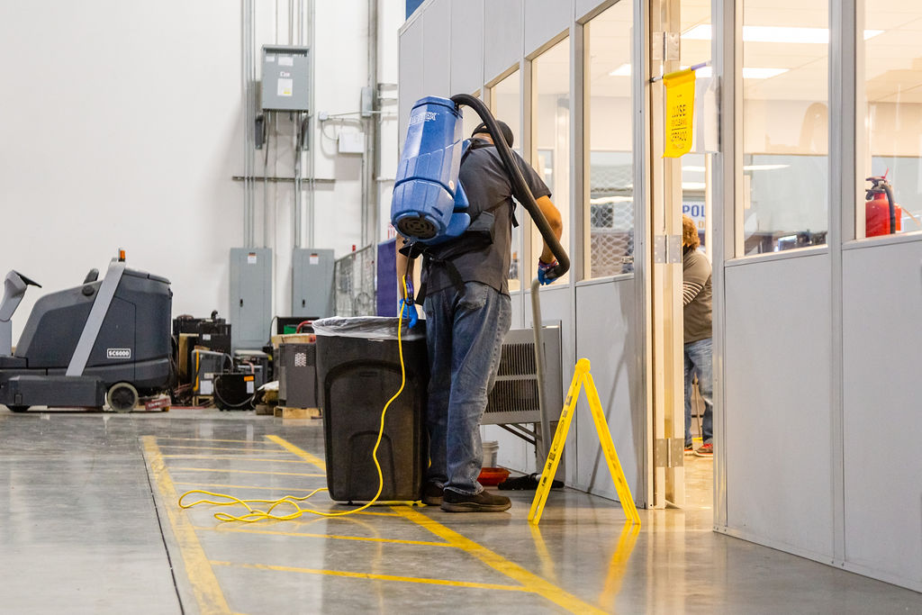 Man cleaning the floor with vacuum cleaner in commercial warehouse